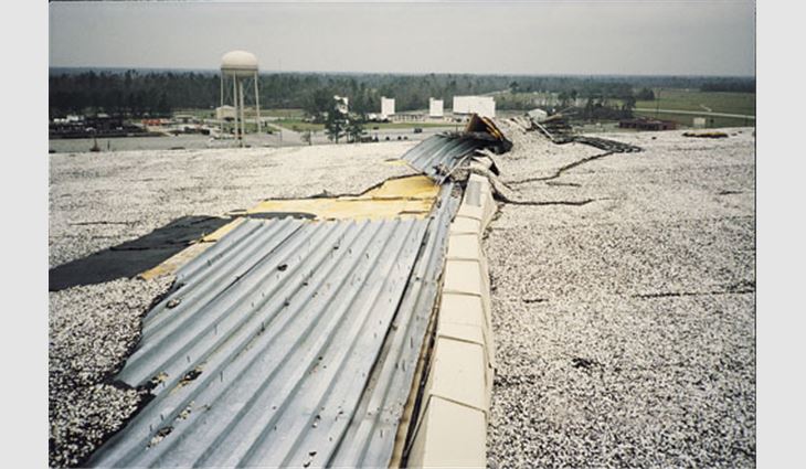This hangar had an aggregate-surfaced built-up membrane over two insulation layers; the first layer was mechanically attached to the deck. The 12-inch- (305-mm-) wide gutter was supported on heavy steel brackets, which rested on and extended out about 4 feet (1 m) onto the deck. The straps were screwed to the deck, but the deck did not have enhanced welding to the support structure to account for the uplift load the gutter transferred to the deck. As a result, large areas of the deck blew off in one corner and along the wall on the opposite side.