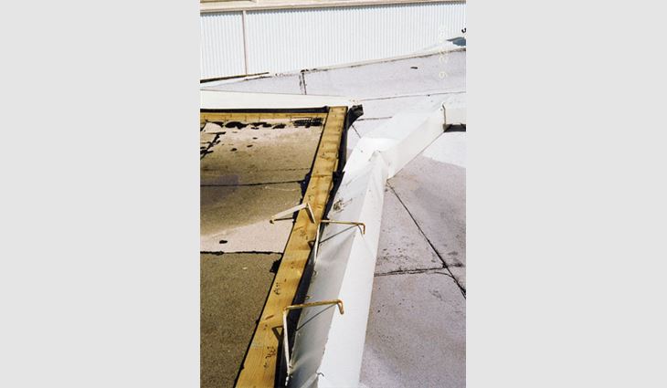 This hangar had a modified bitumen membrane adhered over two insulation layers; the first insulation layer was mechanically attached to the metal deck. The wide gutter was not designed for wind uplift. All the gutter's wind load was transferred to the edge nailer, but the nailer attachment did not account for the additional load. The nailer lifted and caused the roof membrane to peel.