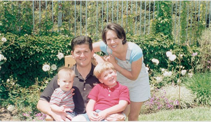 Menzel holding his sons, Brandon (left) and Austin, with his wife, Michelle, in their backyard.