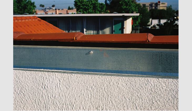 This photo shows a typical parapet wall with SPF and coating applied up the wall to the top of the plate. Galvanized sheet metal was formed and attached as a metal parapet cap with a drip edge. This field detail is topped with clay tile as part of the architectural finish needed. The use of metal as a parapet cap and counterflashing is similar to detail SPF-15 that can be found in <i>The NRCA Roofing and Waterproofing Manual, Fifth Edition</i>. 