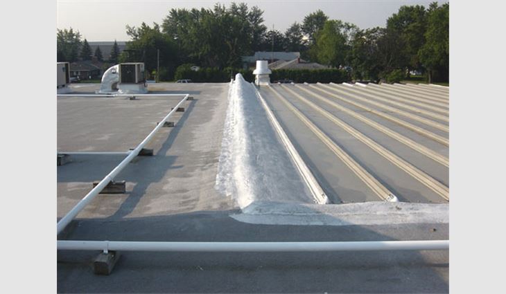 A roof-to-roof transition is shown in this photo, which details how SPF was used to solve a difficult tie-in for two roof systems. The existing metal flashing detail was covered with SPF and coated. The SPF transition detail also makes a right angle and continues to the right as a tie-in to the metal roof system that was added to the existing structure. The SPF tie-in was installed in 1991. 