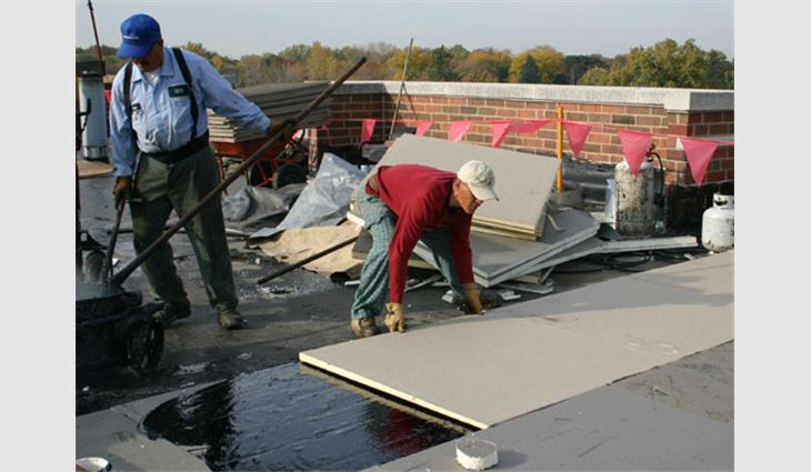 Workers set the tapered insulation in hot asphalt.
