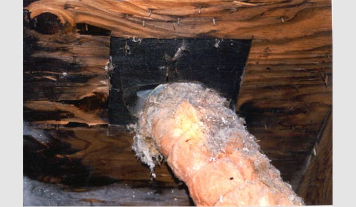 Photo 5: This photo shows conditions at the top end of a vent pipe. The pipe terminated at the bottom of the roof deck, and no clamping device was provided to secure the pipe in position. The top circular edge of the vent was leaning against the sides of the opening cut in the roof deck. The pipe was venting into the attic space rather than to the exterior.
