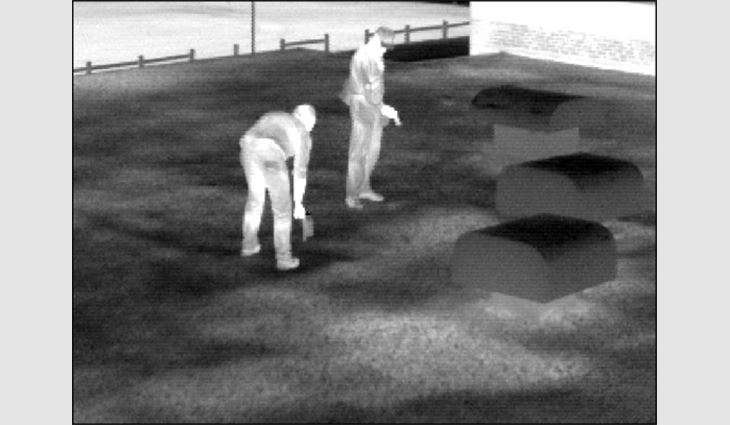 A thermal image of a rooftop inspection shows two people marking the areas of wet insulation, which appear lighter.
