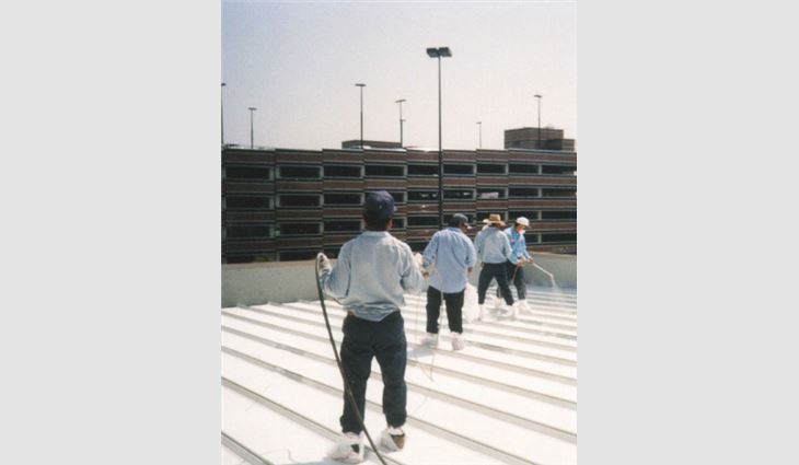 Workers spray a white coating on a metal roof system.