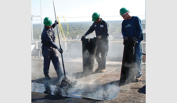 Crew members from Greensboro Roofing Co. Inc., Greensboro, N.C., mop the new roof system in hot asphalt.