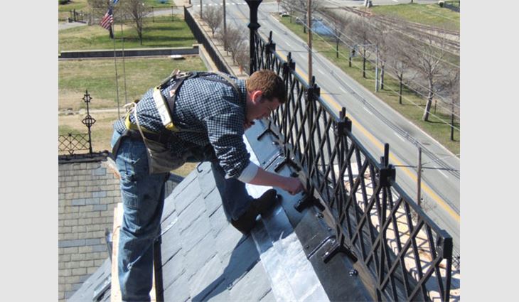 A worker touches up paint on the roof's wrought-iron decorative elements.