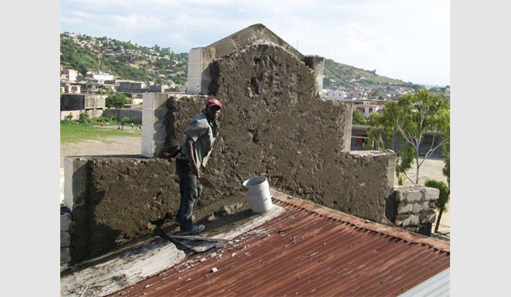 A Haitian worker applies masonry to the rear of an outer parapet wall