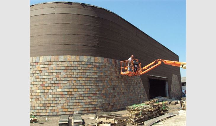 A worker installs slate on the sanctuary's exterior wall from a man-lift