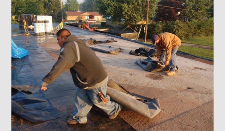Workers remove EPDM membrane from a ballasted roof system. 