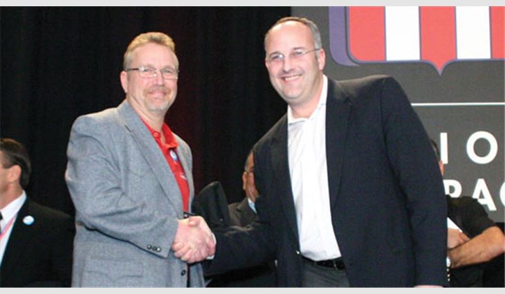 Denton shakes hands with Josh Kelly, vice president and general manager of OMG Roofing Products, Agawam, Mass., and a member of the MVP Task Force, after receiving the Best of the Best Award.
