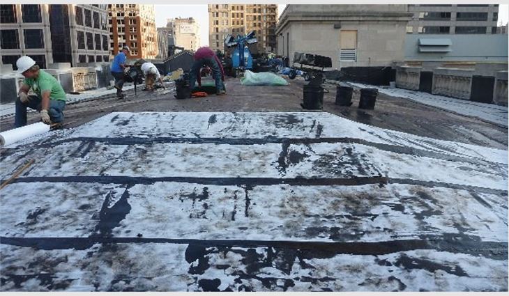 Workers assemble one of multiple layers in a new rubberized asphalt roof system