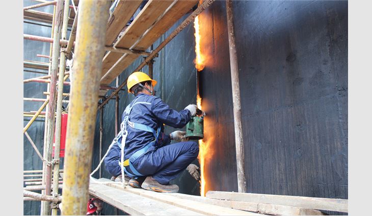 Workers apply a waterproofing membrane using a gas-fired torch.