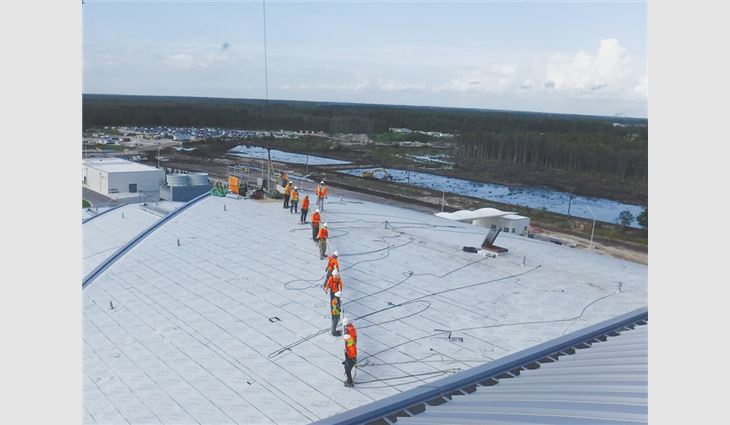 Workers move a roof panel across the rooftop.