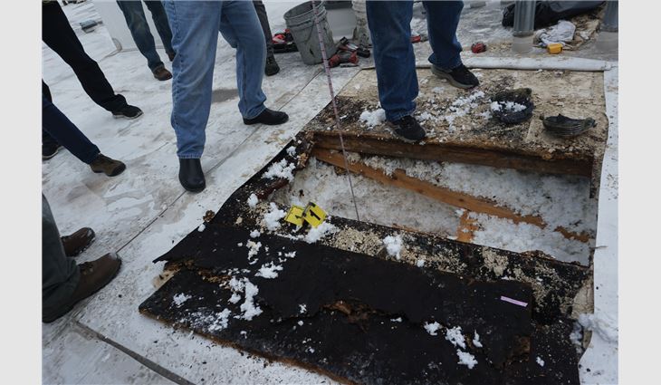 Photo 2: An opening made during an investigation into the cause of soft roof areas. The openings were made in winter. The oriented strand board (black in the foreground) is saturated. This is the same roof system as Photo 1.